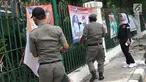 Petugas Satpol PP bersama Panwaslu kecamatan Ciracas menurunkan APK yang terpasang di pagar pembatas antara jalan dengan taman di pinggir kali di sekitar Jalan Raya Bogor, Jakarta, Rabu (23/1). (Liputan6.com/Helmi Fithriansyah)