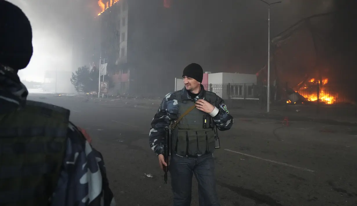 Prajurit Ukraina berjalan saat api dan asap membubung di atas sebuah bangunan setelah penembakan di Kiev, Ukraina, Kamis (3/3/2022). Rusia telah meluncurkan serangan jarak jauh ke Ukraina, menghantam kota dan pangkalan dengan serangan udara atau penembakan. (AP Photo/Efrem Lukatsky)