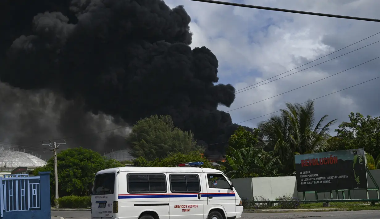 Asap hitam dari kebakaran besar di depot bahan bakar terlihat saat sebuah truk air melewati jalan di Matanzas, Kuba (7/8/2022). Kuba meminta bantuan Sabtu (7/7) untuk mengatasi kebakaran besar yang menyebabkan 77 orang terluka dan 17 petugas pemadam kebakaran hilang. Sekitar 800 orang telah dievakuasi dari daerah tersebut. (AFP/Yamil Lage)