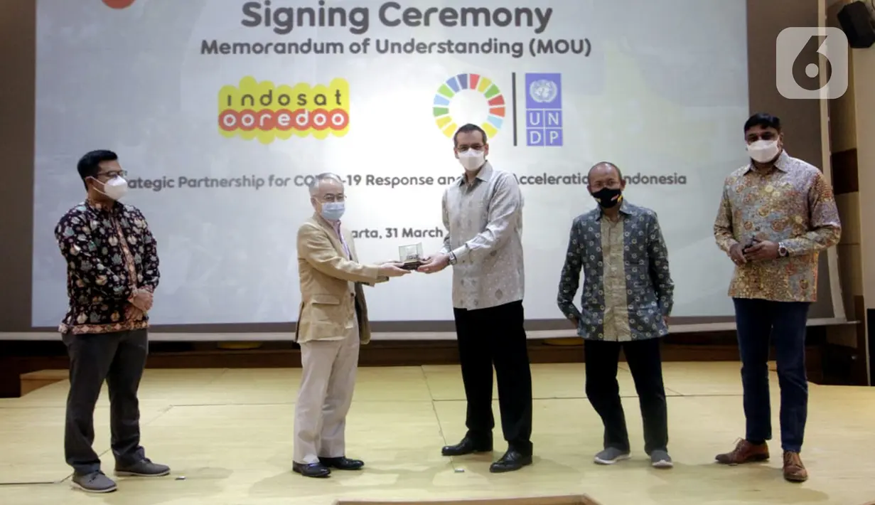 Resident Representative UNDP Indonesia, Norimasa Shimomura (kedua kiri) dan Presdir & CEO Indosat Ooredoo, Ahmad Al-Neama (tengah) bertukar cindermata usai menandatangani MoU penanggulangan pandemi COVID-19 dan percepatan pencapaian SDGs, di Jakarta, Rabu (31/3/2021). (Liputan6.com/Pool/Indosat)
