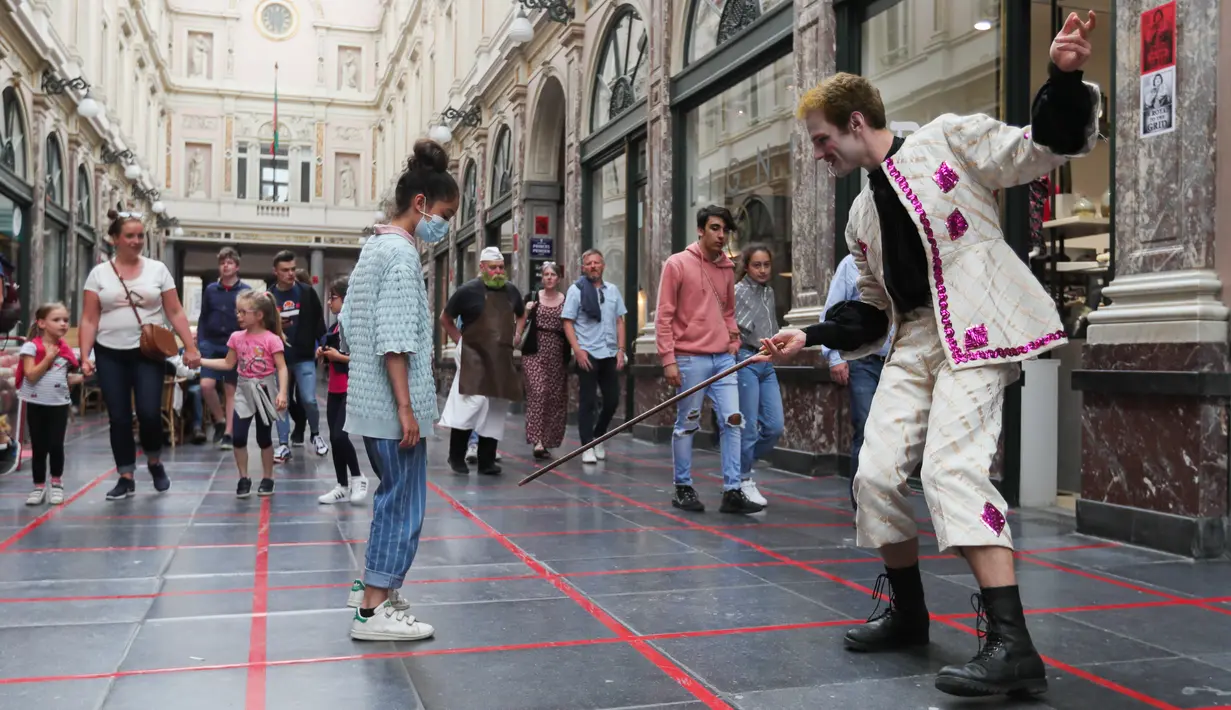 Seorang seniman memainkan permainan dalam garis persegi (grid game) dengan seorang anak gadis di Royal Gallery of Saint Hubert di Brussel, Belgia (15/7/2020). Permainan ini dirancang agar orang menghormati aturan jaga jarak sosial selama pandemi COVID-19. (Xinhua/Zheng Huansong)