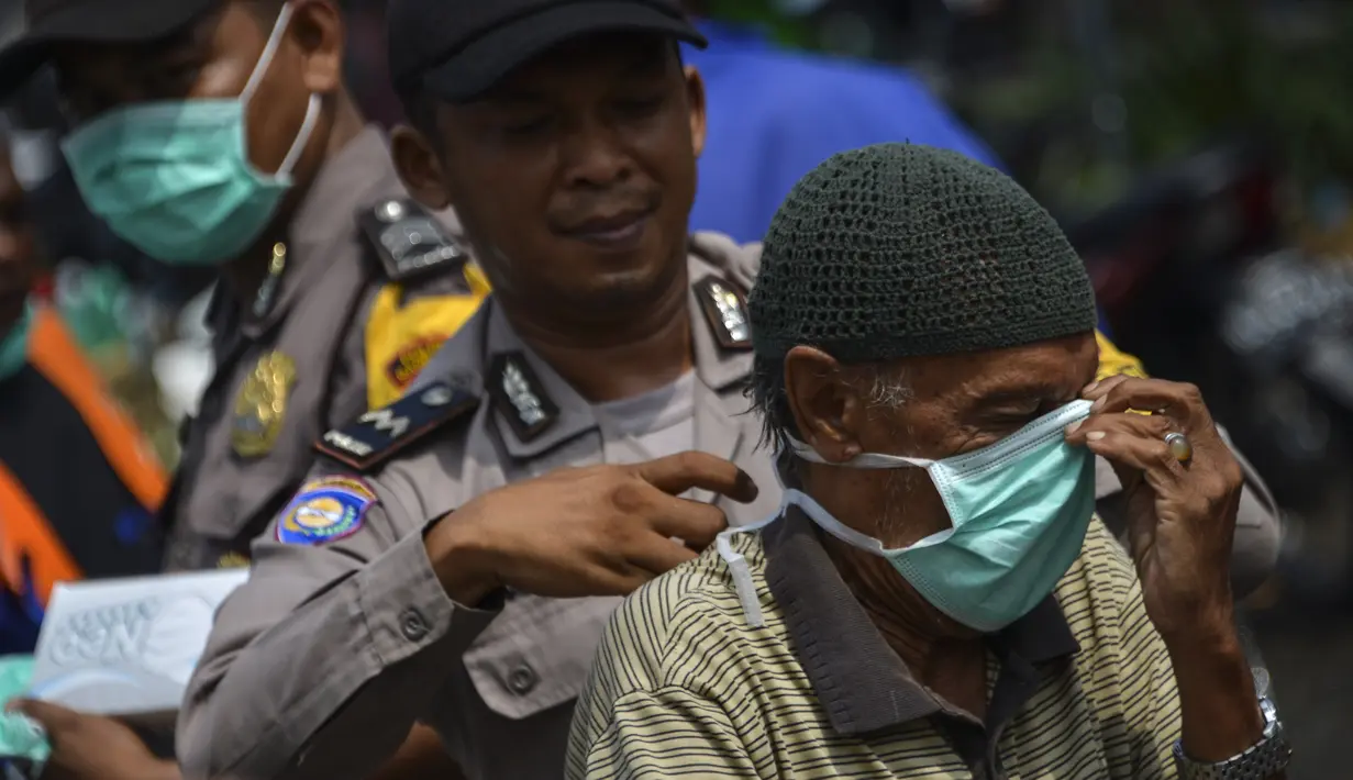 Petugas polisi memasangkan masker kepada warga saat kabut asap tebal menyelimuti wilayah Banda Aceh (25/9/2019). PBB memperingatkan pada 24 September, ketika para ilmuwan mengatakan api melepaskan sejumlah besar gas rumah kaca yang merusak iklim. (AFP Photo/Chaideer Mahyuddin)