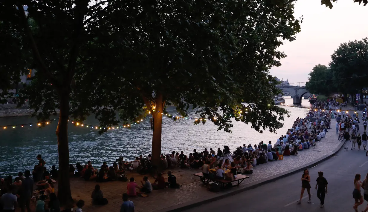 Orang-orang duduk saat berkumpul di tepi sungai Seine sebagai bagian dari acara musim panas Paris Plages di Paris, Prancis (7/7). (AFP Photo/Francois Guillot)