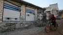 Seorang pria mengendarai sepeda motornya di sepanjang toko-toko yang rusak setelah operasi militer AS di Atmeh, Provinsi Idlib, Suriah, 3 Februari 2022. Pasukan khusus AS melakukan serangan kontraterorisme skala besar yang menewaskan banyak orang di lokasi tersebut. (AP Photo/Ghaith Alsayed)