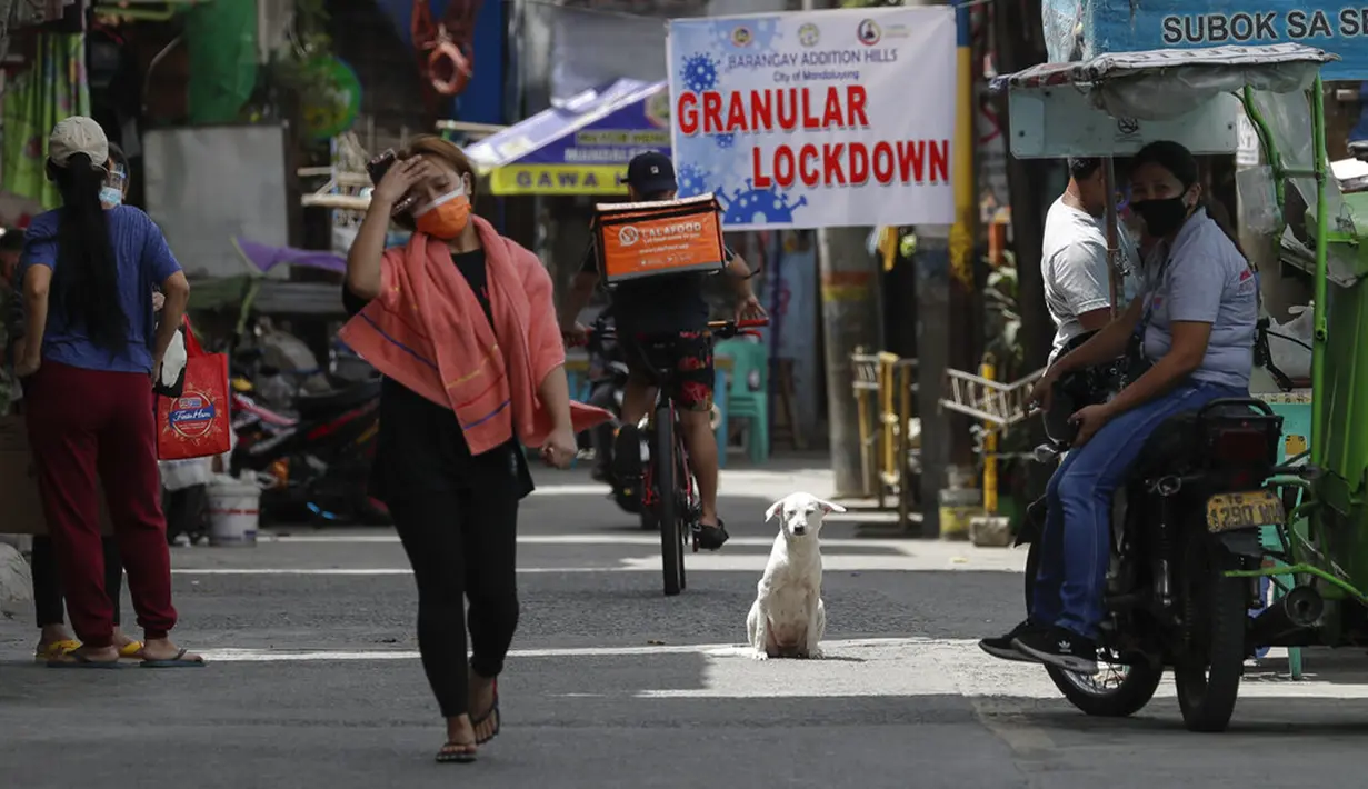 Seekor anjing duduk saat warga berjalan di desa yang dilockdown untuk mencegah penyebaran COVID-19 di Manila, Filipina, Senin (15/3/2021). Lonjakan kasus COVID-19 di Filipina menambah kekhawatiran atas lambannya vaksinasi dan keengganan publik. (AP Photo/Aaron Favila)