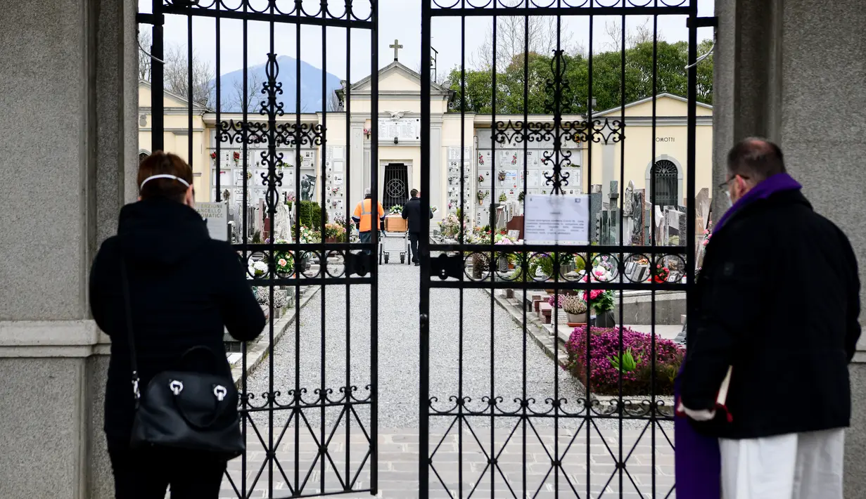 Kerabat dari warga yang sudah meninggal (kiri) dan pendeta melihat peti mati dibawa menuju ke dalam kuburan tertutup Bolgare saat upacara pemakaman selama masa lockdown untuk menghentikan penyebaran pandemi virus corona COVID-19 di Lombardy, Italia, Senin (23/3/2020). (Piero CRUCIATTI / AFP)