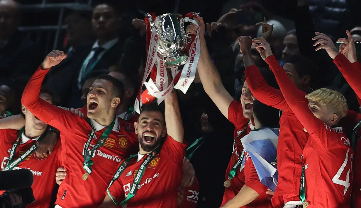 Pemain Manchester United, Bruno Fernandes mengangkat trofi setelah memenangkan final Carabao Cup 2023 melawan Newcastle United yang berlangsung di Wembley Stadium, Minggu (26/2/2023) waktu setempat. (AFP/Adrian Dennis)