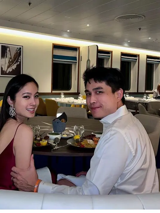 Nong Poy tampil dengan dress satin spaghetti strap warna maroon. Sang suami tampil mengenakan kemeja lengan panjang putih. [@poydtreechada]