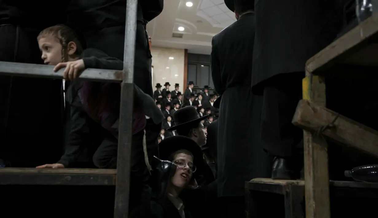 Seorang anak memanjat untuk melihat umat Yahudi ultra-ortodoks dari dinasti Sadigura Hasidic merayakan Hari Raya Tu Bishvat atau Tahun Baru Pohon di Bnei Brak, Israel, 16 Januari 2022. Mereka duduk bersama para rabi di sekitar meja panjang dengan hidangan aneka buah-buahan. (AP Photo/Ariel Schalit)