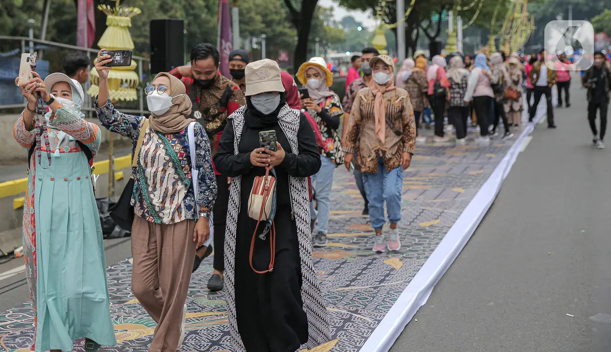 Sejumlah orang yang mengenakan batik mengambil gambar menggunakan gadgetnya saat berjalan di catwalk sepanjang Jalan Jenderal Sudirman, Jakarta, Minggu (2/10/2022). Kegiatan yang diikuti ratusan orang ini diselenggarakan oleh Bank Mandiri untuk menyambut Hari Batik Nasional yang jatuh setiap tanggal 2 Oktober 2022. (Liputan6.com/Faizal Fanani)