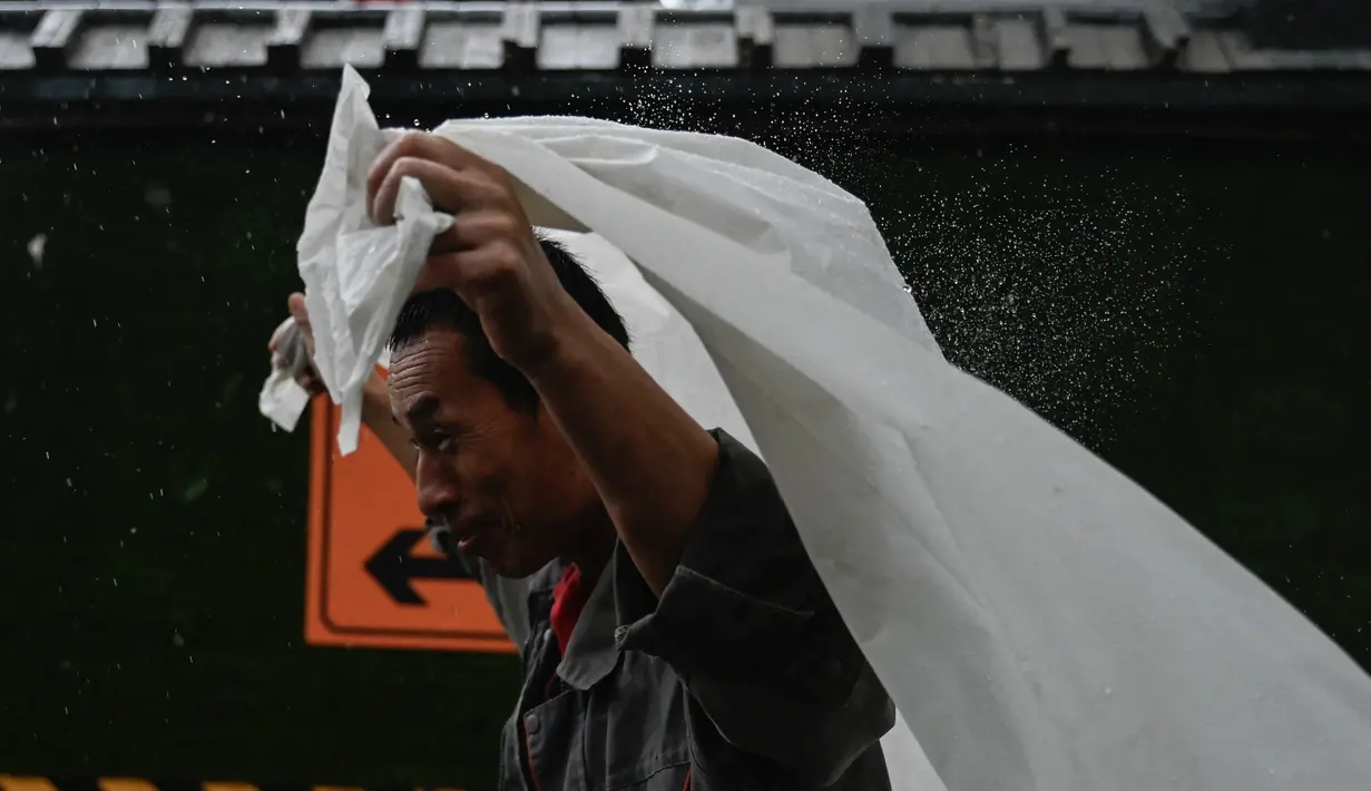 Seorang pria berlindung dari hujan dengan selembar plastik di Beijing, Minggu (30/7/2023). China menempatkan sebagian wilayah utara negara tersebut dalam keadaan siaga merah, termasuk wilayah Beijing, karena hujan lebat yang diperkirakan akan terjadi akibat datangnya topan Doksuri, yang saat ini menghantam bagian lain negara tersebut. (Pedro PARDO / AFP)