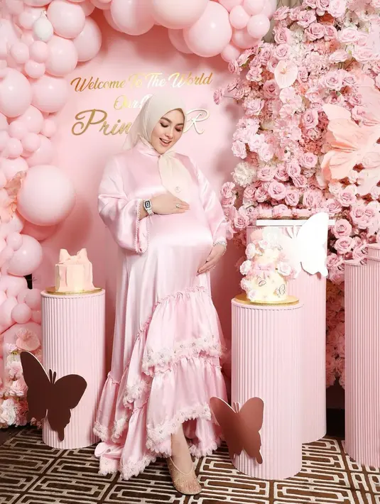 Pada look pertama, Syahrini mengenakan gaun panjang berwarna pink pastel dengan aksen ruffle di bagian bawahnya. Gaunnya tersebut dipadukan dengan hijab segi empat berwarna nude pink.  [@princessyahrini].