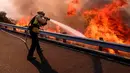 Petugas pemadam kebakaran berusaha memadamkan api di sepanjang Ronald Reagan (118) di Simi Valley, Californnia (12/11). Api Woolsey menjalar ke jalan raya dan menuju kota pesisir, termasuk kawasan wisata Malibu dan Calabasas. (AP Photo/Ringo H.W. Chiu)