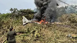 Pesawat berjenis C-130 Hercules itu jatuh tak lama setelah lepas landas dari Puerto Leguizamo, Kolombia, menyebarkan puing-puing yang terbakar di dasar hutan. Tampak dalam foto, kobaran api dan asap hitam tebal membubung dari pesawat Hercules Angkatan Udara yang jatuh saat lepas landas, sementara seorang anggota Kepolisian Kolombia berdiri di dekatnya, di Puerto Leguizamo, Kolombia, pada Senin 23 Maret 2026. (Daniel Ortiz/AFP)