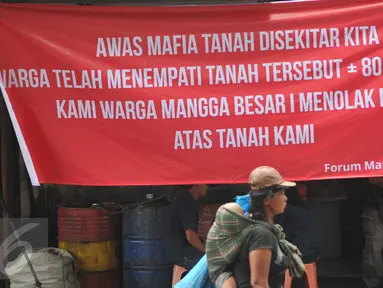Seorang ibu menggendong anaknya berjalan di depan spanduk penolakan di kawasan jalan Mangga Besar, Jakarta, Senin (22/8). Spanduk itu dipasang warga RW2 Kelurahan Mangga Besar sebagai aksi menolak penggusuran rumah mereka. (Liputan6.com/Gempur M Surya)