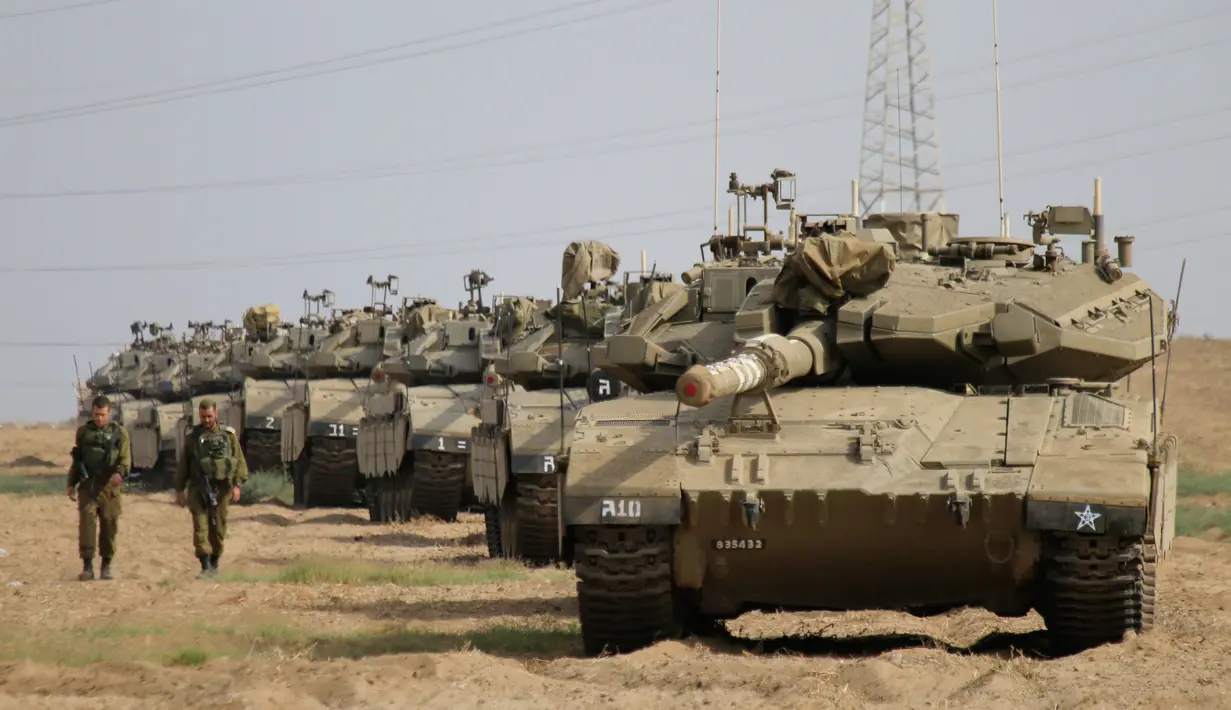 Tentara Israel berjalan melewati tank di dekat perbatasan Gaza-Israel, Jumat (19/10). Sekitar 60 tank dan kendaraan lapis baja pengangkut personel bergerak melalui jalan-jalan Israel menuju perbatasan Gaza. (AP Photo/Ariel Schalit)