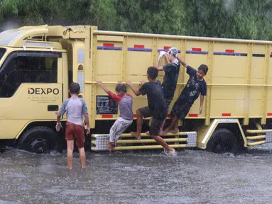 Sejumlah anak menaiki truk saat bermain banjir di jalan Bayangkara Pusdiklat, Kota Tangerang Selatan, Banten, Selasa (2/11/2021). Aksi anak anak tersebut dapat membahayakan keselamatan jiwa karena banyaknya kendaraan yang melintas menerjang banjir. (Liputan6.com/Angga Yuniar)