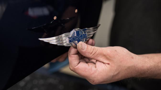 Pekerja menunjukkan logo perusahan ke bagian bodywork mobil  di pabrik Morgan Motor Company di Malvern, Birmingham, Inggris (13/8/2019). Morgan Motor Company telah memproduksi kendaraan klasik Inggris selama lebih dari 105 tahun. (AFP Photo/Oli Scarff)