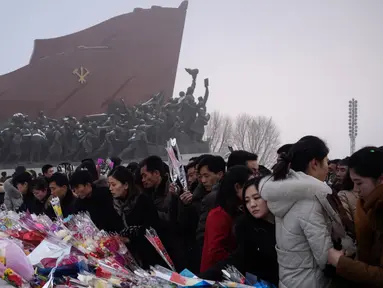 Penduduk Pyongyang meletakkan bunga di depan patung pemimpin Korea Utara Kim Il Sung dan Kim Jong Il selama Hari Peringatan Nasional di Bukit Mansu, Pyongyang (17/12).  Korea Utara tengah memperingati 7 tahun wafatnya  Kim Jong Il. (AFP Photo/Kim Won Jin)