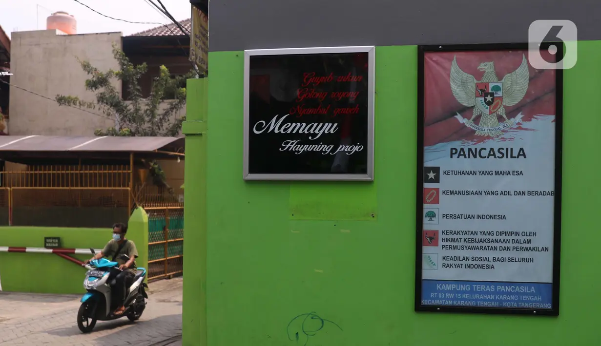 Warga melintas di sebelah papan berisikan poin-poin pancasila di Kampung Pancasila, Karang Tengah, Kota Tangerang, Selasa (1/6/2021). Kegiatan tersebut antara lain seperti gotong royong membersihkan kampung dan sosialisasi penanaman nilai Pancasila kepada warga . (Liputan6.com/Angga Yuniar)