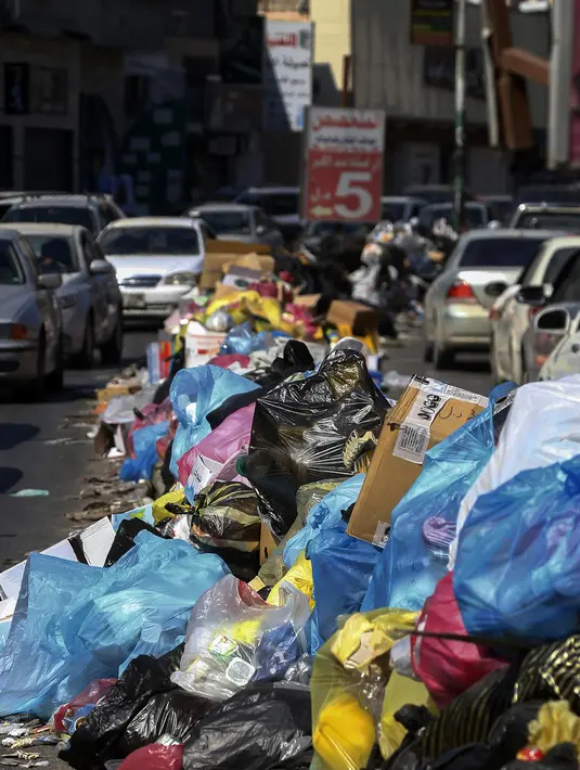 Kendaraan melintas di samping tumpukan sampah di sepanjang sisi jalan di Tripoli, ibukota Libya (30/9/2019). Truk sampah kota tidak lagi mengumpulkan sampah karena TPA utama kota ada di garis depan. (AFP Photo/Mahmud Turkia)
