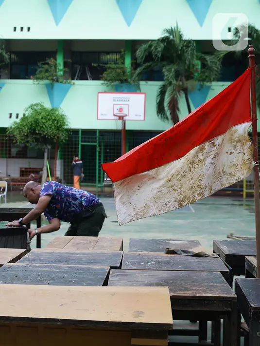 Guru membersihkan meja pascabanjir yang merendam SMA Negeri 8 Jakarta di Bukit Duri, Tebet, Jakarta, Sabtu (4/1/2020). Data Kemendikbud menyebutkan per 3 Januari 2020 terdapat 290 sekolah terdampak banjir di wilayah DKI Jakarta. (Liputan6.com/Herman Zakharia)