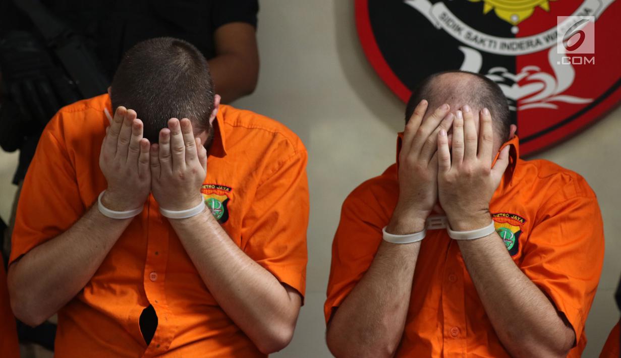 Dua tersangka pembobol uang dari mesin ATM dengan teknik skimming menutup wajah saat diperlihatkan petugas Resmob Polda Metro Jaya di Jakarta, Sabtu (17/3). Sindikat ini membobol 64 bank pada sejumlah negara. (Liputan6.com/Helmi Fithriansyah)