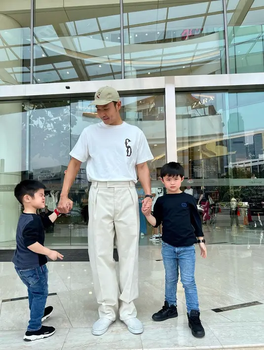 Penampilan serasi Harvey Moeis bersama kedua anak laki-lakinya; Raphael dan Mikhael Moeis. Harvey mengenakan kaus lengan pendek putih yang dimasukkan ke dalam celana panjang beige-nya dan topi cokelat muda. Sedangkan kedua anak laki-lakinya mengenakan outfit kembar atasan lengan panjang berwarna hitam dan celana jeans panjang, serta sneakers hitam. [Foto: Instagram/raphaelmoeis]