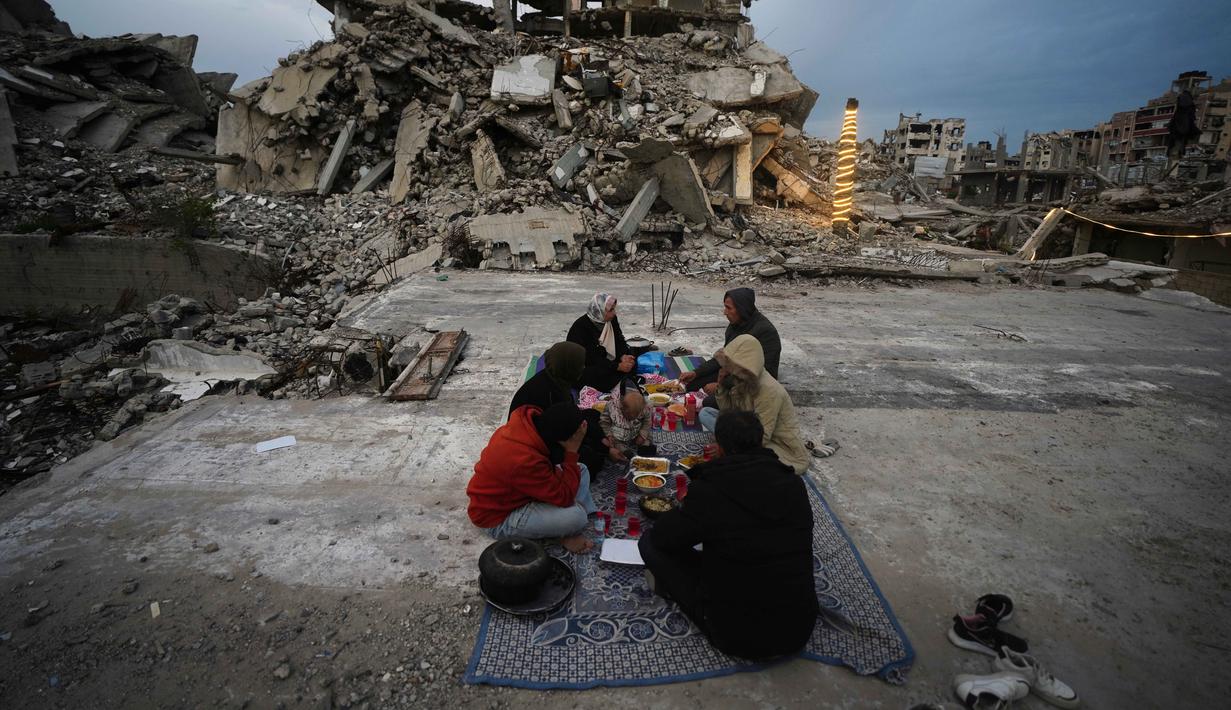 Bagi banyak warga di Gaza, Ramadan tahun ini dijalani dalam kondisi yang jauh lebih sulit. Banyak keluarga kehilangan tempat tinggal akibat serangan udara yang merusak rumah-rumah dan infrastruktur sipil. Tampak dalam foto, anggota keluarga Al-Najar berbuka puasa selama bulan suci Ramadan di tengah reruntuhan bangunan yang hancur di Kota Gaza, Jumat 13 Maret 2026. (AP Photo/Jehad Alshrafi)