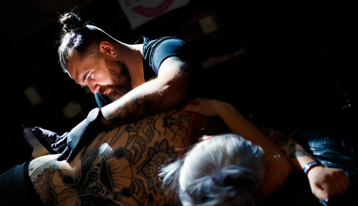 Seorang seniman  mentato badan pengunjung wanita dalam acara edisi keempat Montreux Tattoo Convention di Montreux, Swiss  (22/9). Montreux Tattoo Convention berlangsung selama tiga hari. (Valentin Flauraud/Keystone via AP)