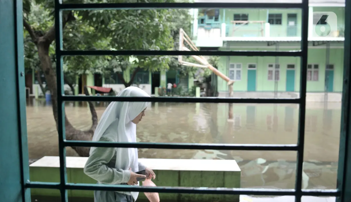 Murid melintas di depan ruang kelas saat banjir menggenangi Madrasah Tsanawiyah (MTs) Nur Attaqwa, Pegangsaan Dua, Kelapa Gading, Jakarta Utara, Senin (24/2/2020). Banjir sejak Minggu (23/2) kemarin mengakibatkan kegiatan belajar di MTs itu terpaksa diliburkan. (merdeka.com/Iqbal S Nugroho)