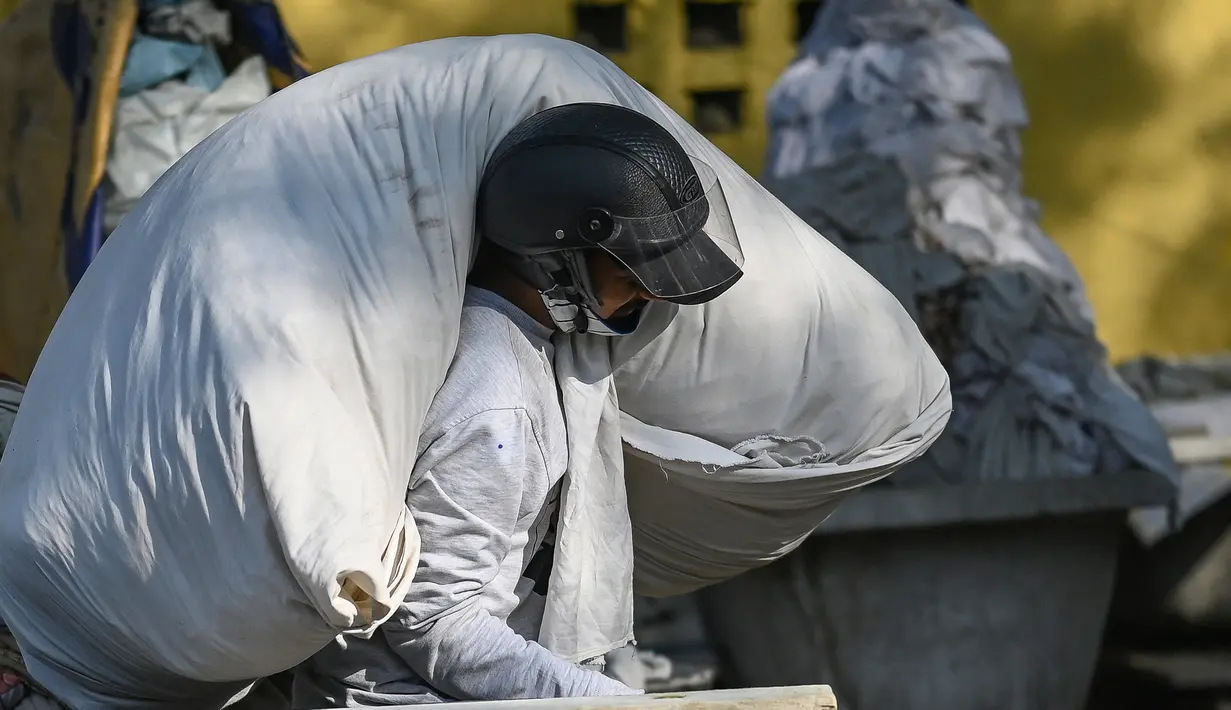 Seorang tukang cuci membawa pakaian untuk dicuci di binatu terbuka, yang secara lokal disebut 'Dhobi Ghat' di New Delhi, India pada 14 Maret 2022. Dhobi Ghat adalah tempat yang menyediakan layanan cuci dengan cara tradisional. (Money SHARMA / AFP)