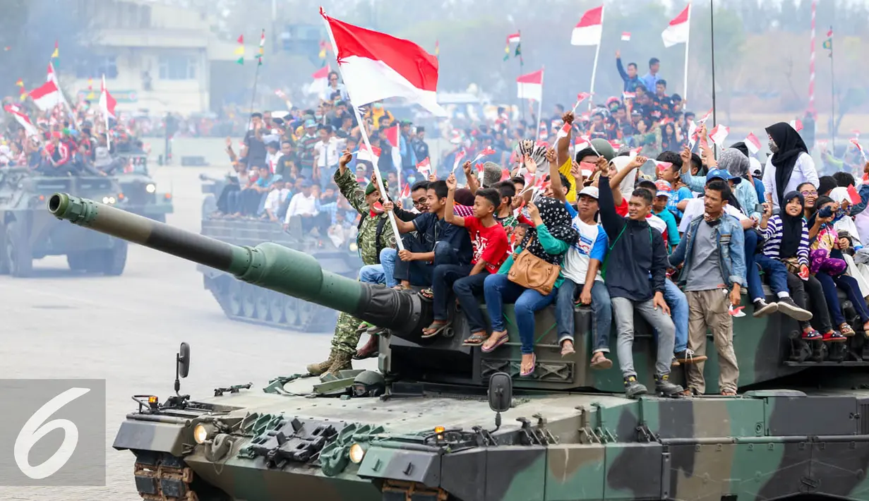 Warga membawa bendera merah putih saat menaiki tank TNI menyaksikan HUT TNI ke-70 di Dermaga Indah Kiat, Cilegon, Banten, Senin (5/10/2015). HUT TNI Ke-70 ditandai atraksi tempur tiga matra TNI Angkata Darat, Laut dan Udara. (Liputan6.com/Faisal Fanani)