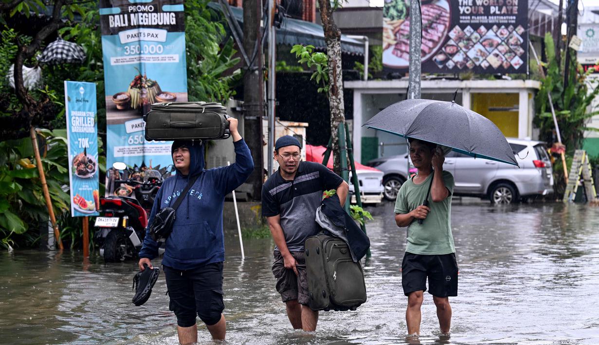 Banjir diakibatkan oleh tingginya curah hujan yang mengguyur pulau Bali sejak Minggu (22/2/2026). Tampak dalam foto, para tamu hotel membawa koper mereka sambil menerobos air di jalan yang tergenang banjir akibat hujan lebat di Legian Kuta, Denpasar, Bali, pada Selasa 24 Februari 2026. ((SONNY TUMBELAKA/AFP)