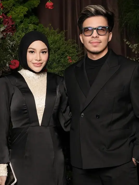 Aurel Hermansyah mengenakan long dress hitam dengan aksen putih di bagian dada dipadukan kerudung hitam polos. Didampingi Atta yang mengenakan jas hitam. [@aurelie.hermansyah]