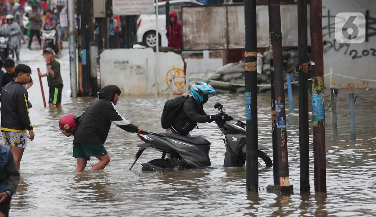 Pengendara motor mendorong kendaraannya melintasi genangan air ketika banjir merendam Jalan KH. Hasyim Ashari, Tangerang, Banten, Sabtu (16/7/2022). Hujan deras mengguyur sejak Jumat siang hingga Sabtu pagi. (Liputan6.com/Angga Yuniar)
