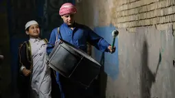 Biasanya mesaharati membawa genderang kecil (tambur) yang ditabuh secara ritmis sambil menyerukan kalimat-kalimat pengingat. Tampak dalam foto, Wissam Ali, seorang "mesaharati" atau penyeru subuh berusia 22 tahun, saat membangunkan orang-orang untuk makan sebelum matahari terbit, selama bulan suci Ramadan, di lingkungan miskin distrik Fadhil di Baghdad, Irak, Senin 23 Februari 2026. (AP Photo/Hadi Mizban)