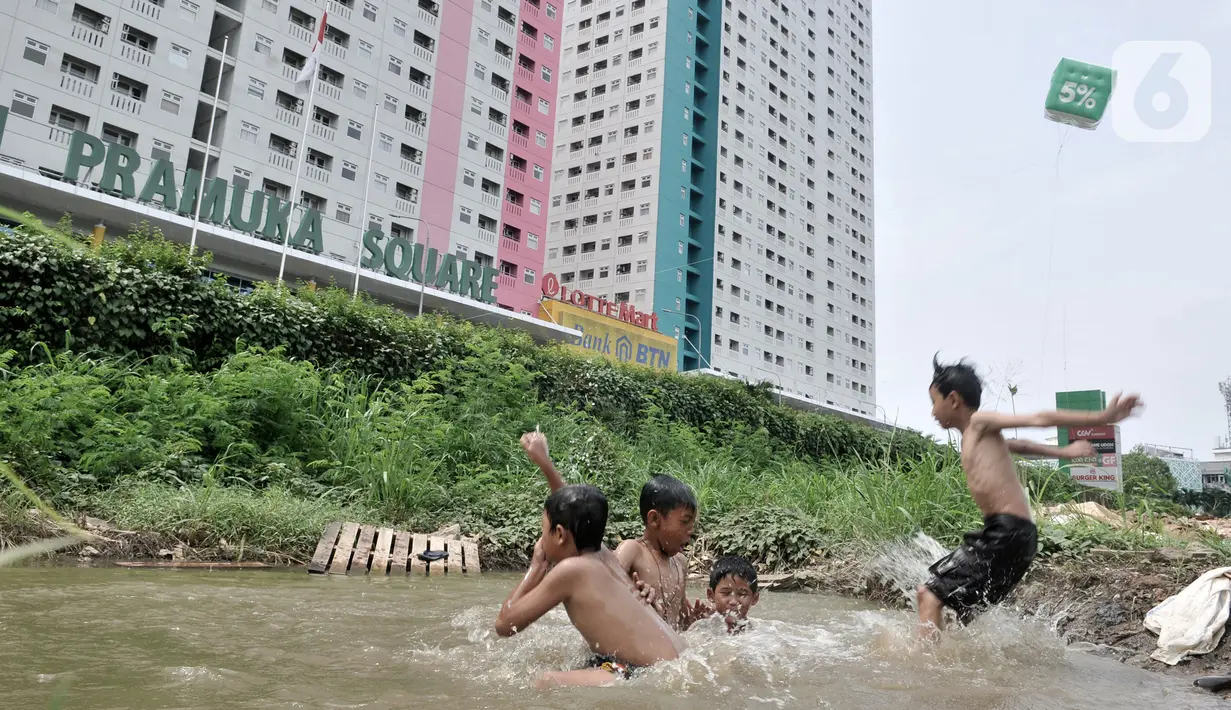 Anak-anak berenang di kubangan air di depan Apartemen Green Pramuka, Jakarta, Rabu (5/2/2020). Keterbatasan ekonomi dan minimnya lahan bermain membuat sekelompok anak sekolah dasar ini memilih berenang di kubangan meskipun mereka tahu air kotor dapat menimbulkan penyakit. (merdeka.com/Iqbal Nugroho)