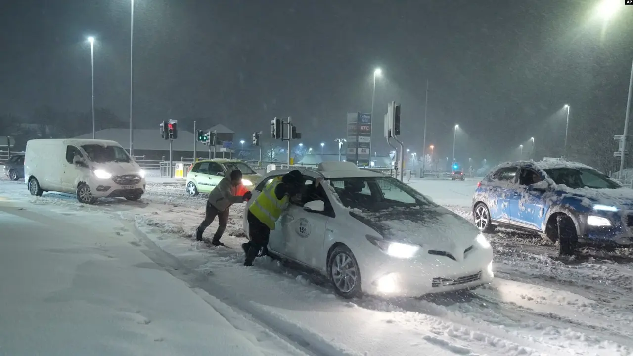 Sejumlah warga mendorong mobil yang terjebak di jalanan bersalju di Leeds, Inggris, pada 5 Januari 2025. (AP)