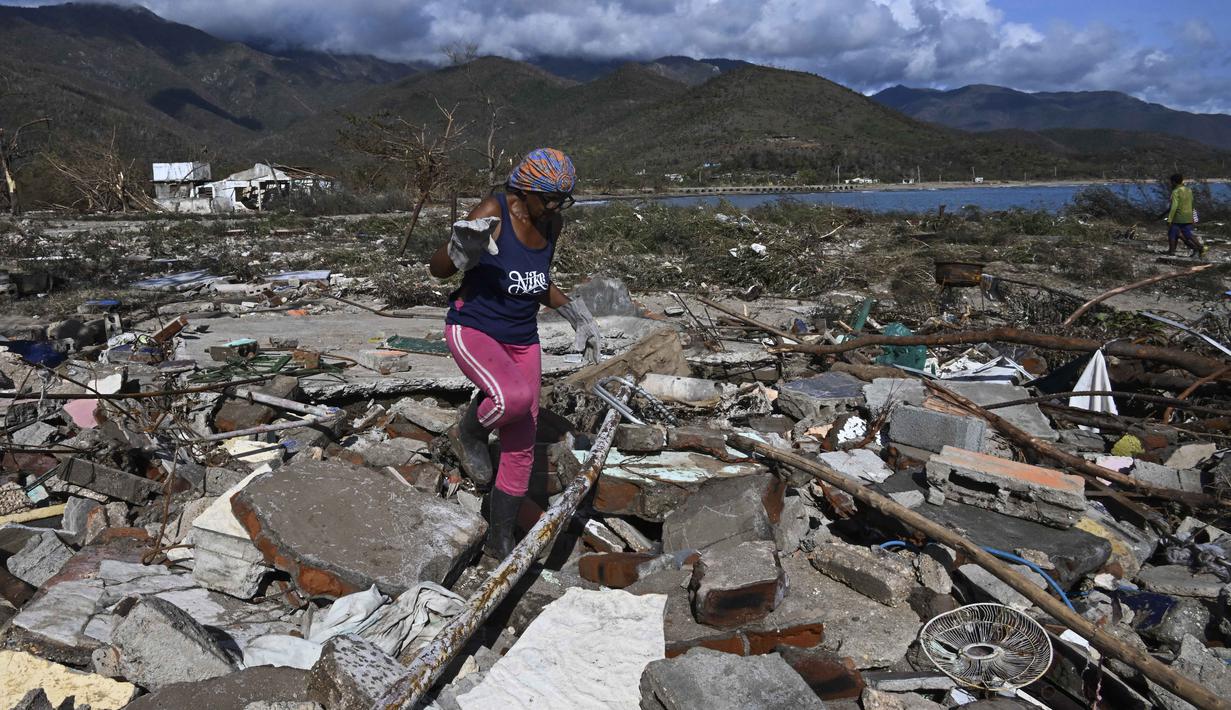 Seorang perempuan berjalan di tengah puing-puing rumah yang rusak akibat Badai Melissa di desa Boca de Dos Rios, provinsi Santiago de Cuba, Kuba pada Kamis 30 Oktober 2025. Badai Melissa sebagai badai Kategori 3 menghantam daratan Kuba pada Rabu (29/10/2025), pagi waktu setempat. (YAMIL LAGE/AFP)