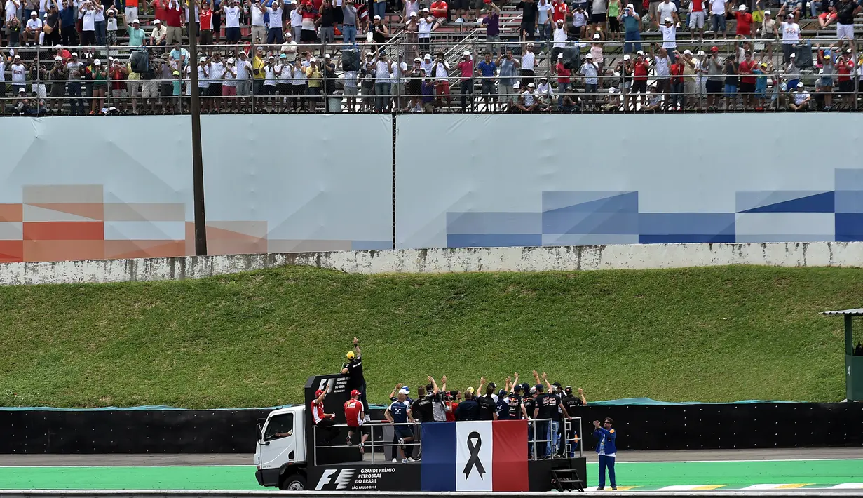 Para pebalap F1 mengikuti parade dengan truk yang dipasangi bendera Prancis sebagai tanda duka terhadap para korban serangan teroris sebelum dimulainya start F1 GP Brasil di Sirkuit Interlagos, Sao Paulo, Brasil, (15/11/2015). (AFP Photo/Nelson Almeida)