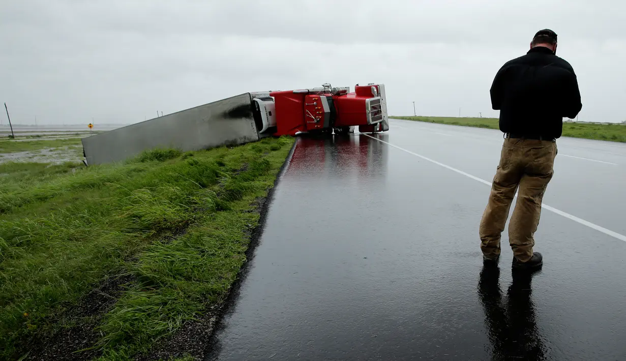 Pengendara berhenti untuk melihat sebuah truk yang terbalik akibat hantaman Badai Harvey di utara Victoria, Texas, Minggu (27/8). Selain menghancurkan bangunan dan rumah, badai yang juga memicu banjir ini merusak banyak fasilitas umum (AP/Charlie Riedel) 