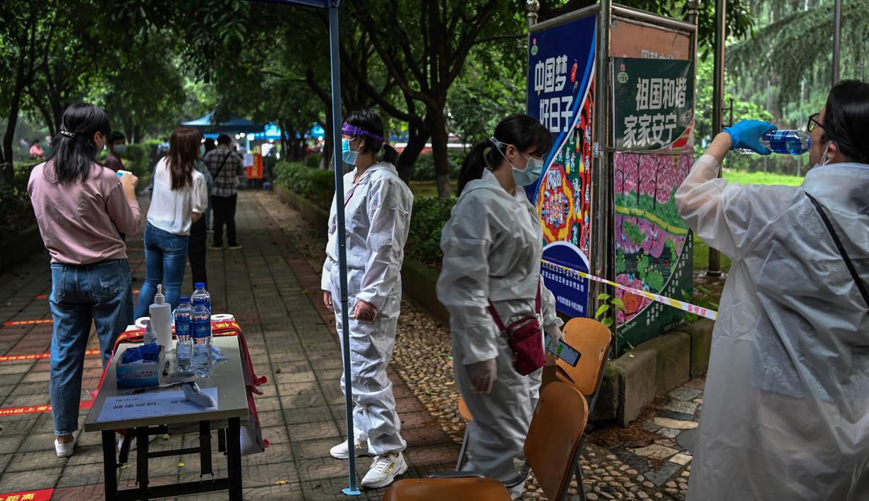 Petugas berdiri di sebelah warga yang menunggu untuk tes virus corona di lingkungan di Wuhan, provinsi Hubei, Jumat (15/5/2020). Tes massal yang ditargetkan dalam 10 hari ini akibat adanya pasien Virus Corona baru di Wuhan, setelah sebulan lebih tidak ada laporan kasus baru. (Hector RETAMAL/AFP)