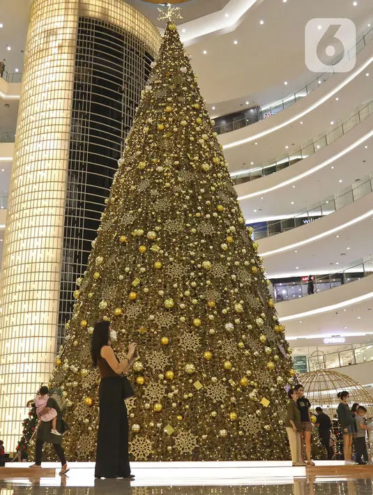 Pengunjung melintas di dekat pohon Natal di Senayan City, Jakarta, Selasa (14/12/2021). Senayan City menghadirkan  Giant Golden Christmas Tree instalasi yang berdiri megah sebagai ikonik momen Natal dengan tinggi mencapai 18 meter dan dikelilingi oleh Golden Christmas Balls. (Liputan6.com/Fai
