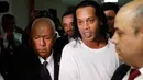 Mantan pemain timnas Brasil, Ronaldinho dikawal oleh polisi meninggalkan kantor pengadilan di Asuncion, ibu kota Paraguay, Jumat (6/3/2020). Ronaldinho bersama saudara laki-lakinya berurusan dengan pihak berwenang Paraguay karena menggunakan paspor palsu untuk memasuki negara itu. (AP/Jorge Saenz)