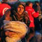 Seorang ibu yang dievakuasi membawa bantuan makanan dari lembaga kemanusiaan di kota al-Rasyidin, Suriah (15/12). Ribuan warga telah dievakuasi di kota yang kini porak-poranda. (REUTERS/Ammar Abdullah)