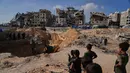 Warga Palestina menyaksikan aktivitas pekerja Mesir yang menggunakan alat berat untuk mencari jenazah para sandera di Kota Hamad, Khan Younis, di Jalur Gaza selatan, Selasa 28 Oktober 2025. (AP Photo/Abdel Kareem Hana)