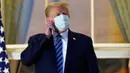 Presiden AS Donald Trump melepas maskernya saat berdiri di balkon di luar Blue Room setelah kembali ke Gedung Putih, Washington, Senin (5/10/2020). Donald Trump meninggalkan Walter Reed National Military Medical Center, rumah sakit tempat dia menjalani perawatan COVID-19. (AP Photo/Alex Brandon)
