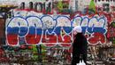 Seorang perempuan berjalan melewati grafiti bertuliskan "Rusia" dengan warna bendera tiga warna Rusia di "Tembok Tsoi" di pusat kota Moskow pada 7 Desember 2023. (NATALIA KOLESNIKOVA/AFP)