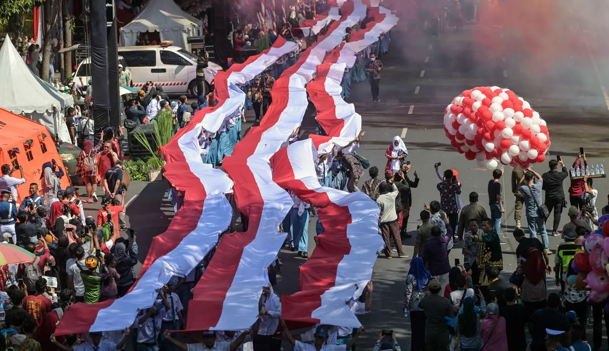 Para siswa dari berbagai sekolah membentangkan bendera Merah Putih panjang saat berbaris di jalan-jalan selama acara upacara untuk memperingati HUT ke-80 Kemerdekaan Indonesia di Surabaya, Jawa Timur pada 17 Agustus 2025. (Juni KRISWANTO/AFP)